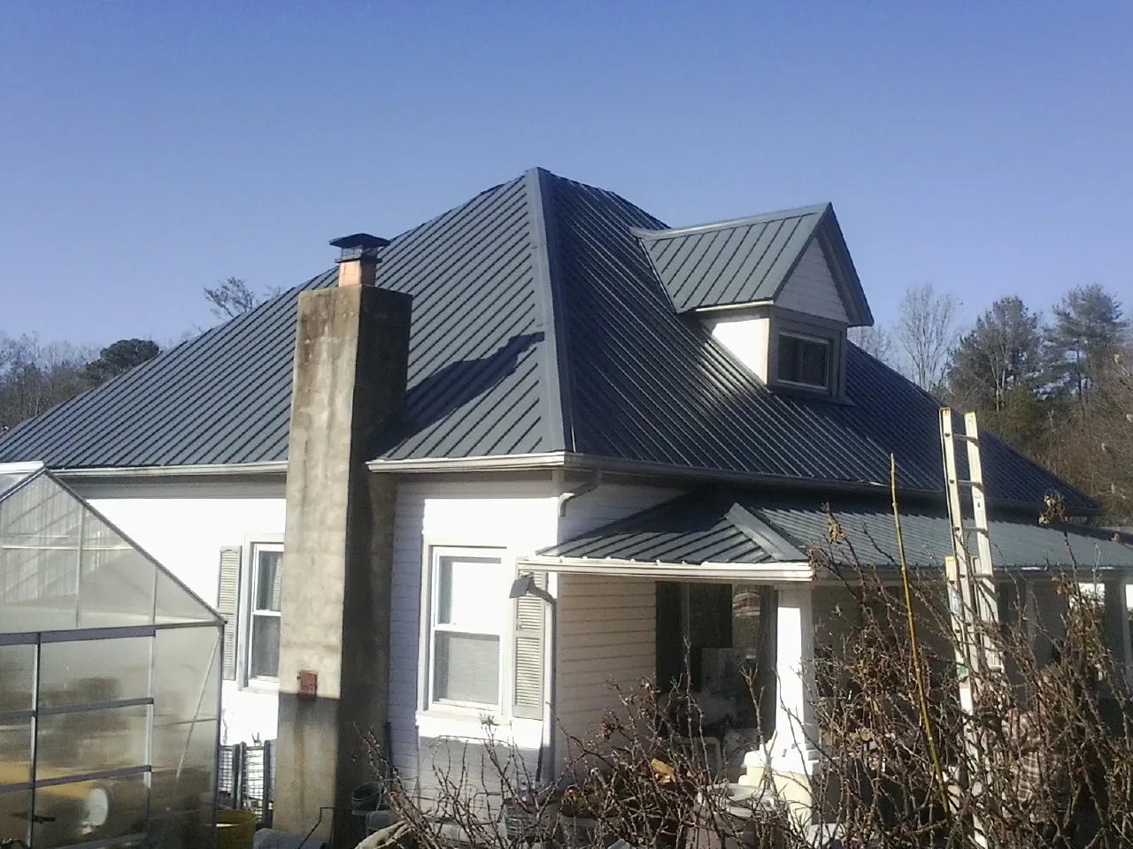 Dark blue standing seam metal roof on a white farmhouse with dormer — Slate & Tile Roof Repair by Roofing Brothers in Leroy