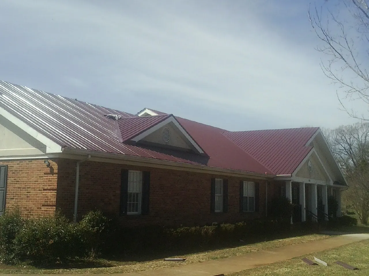 Red metal roof with gabled entries on a long brick building, from a Hail Damage Roof Repair job in Leroy