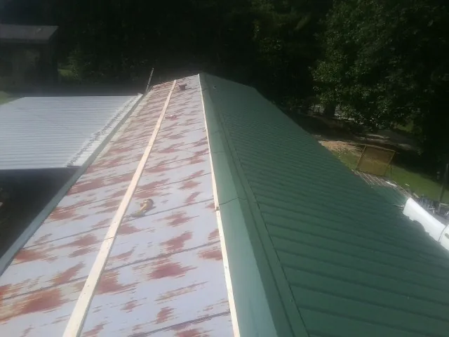 Old rusted panels beside newly installed green metal roofing — Wind Damage Roof Repair by Roofing Brothers in Leroy