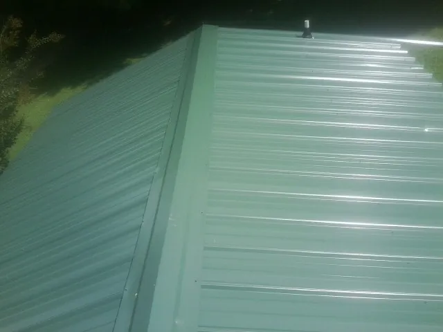 New green metal panels meeting at the ridge of a roof — Flat Roof Repair work by our crew in Leroy