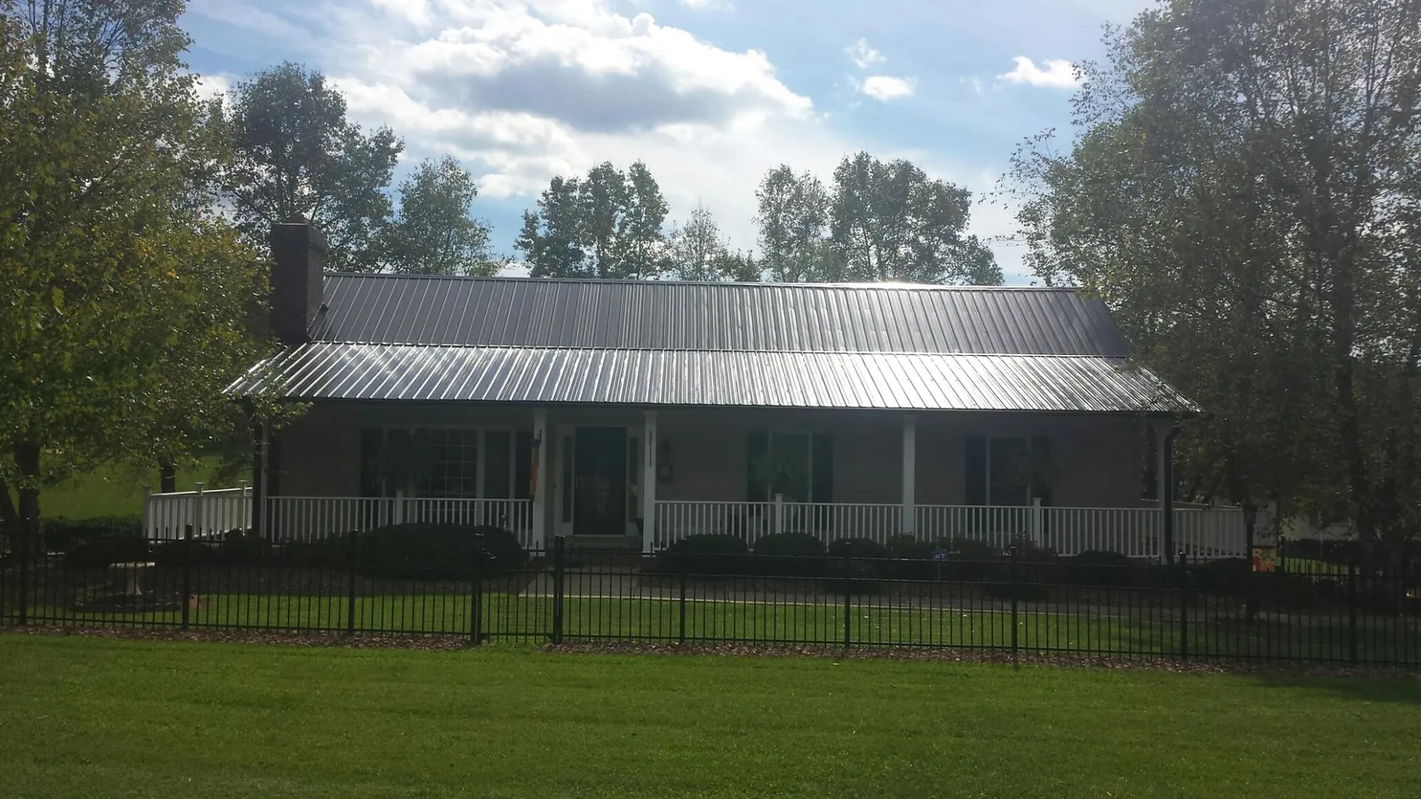 Gray metal roof on a brick ranch with a full width front porch — Gutter Guard Installation work by our crew in Leroy