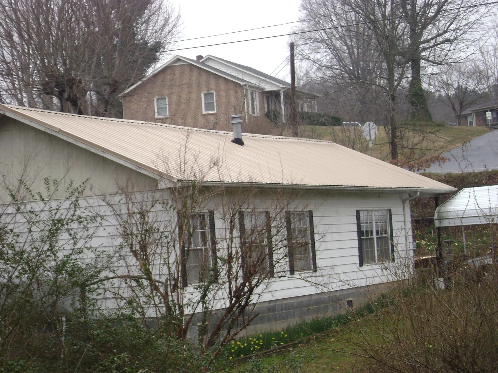 Tan metal roof on a white sided house set into a hillside — Commercial Roofing by Roofing Brothers in Leroy