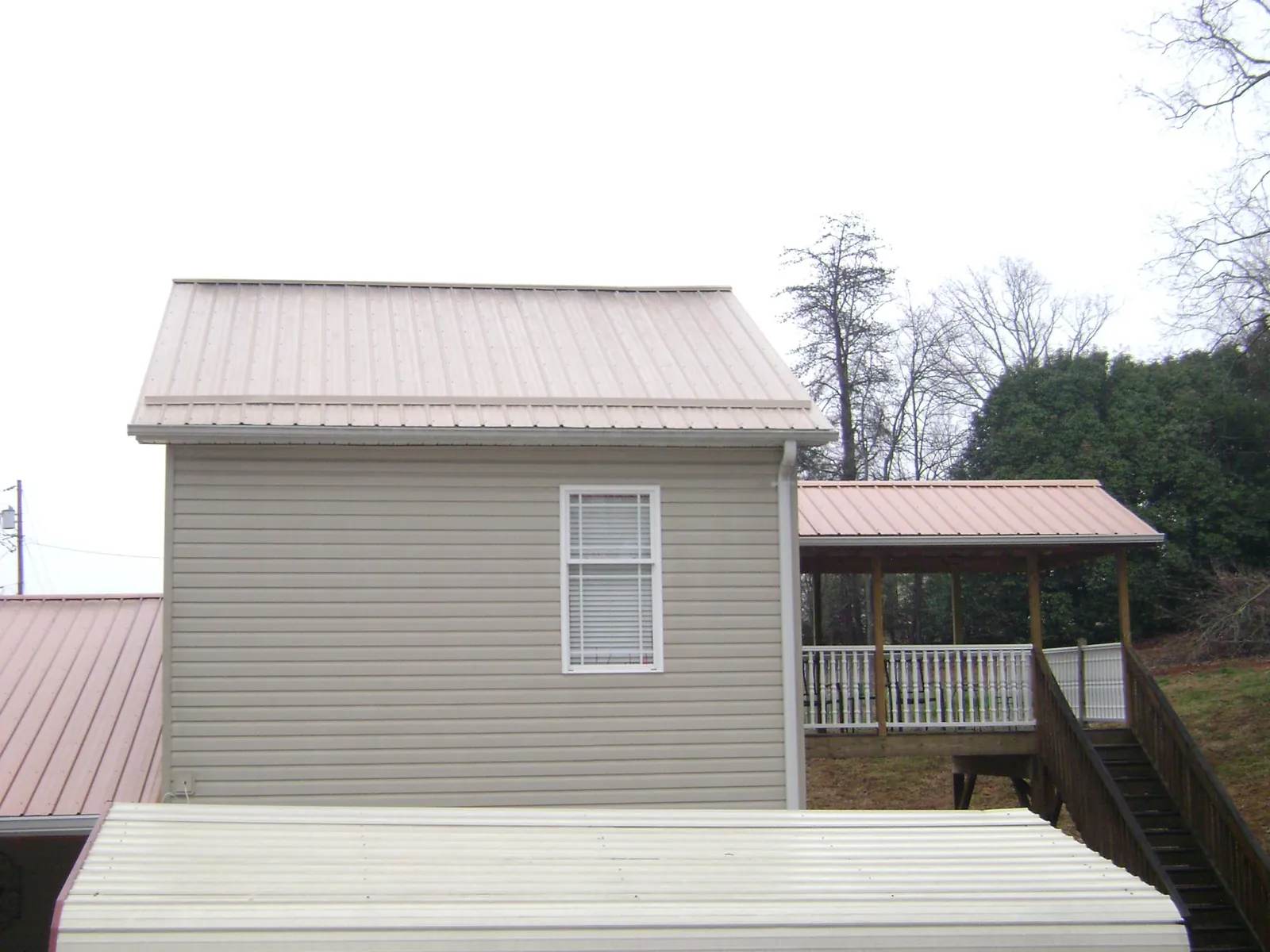 Tan metal roofs on a two story addition and attached porch, from a Roof Replacement job in Leroy